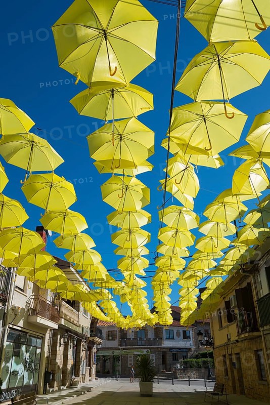 A street under a sky of yellow umbrellas that form an artistic installation on a sunny day, historic centre, Los Molinos, Cuenca del Guadarrama, Madrid, Spain, Europe