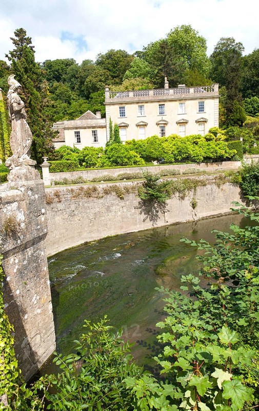 Classical facade of Iford Manor, Bradford on Avon, Wiltshire, England with a statue of Britannia on the fifteenth century bridge over the River Frome