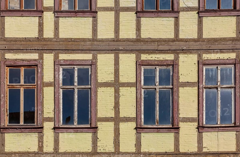Façade of a historic half-timbered building with yellow walls and several rectangular windows with wooden frames, Quedlinburg, Saxony-Anhalt, Germany, Europe