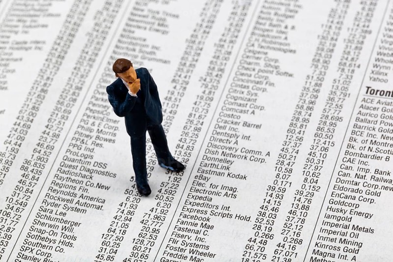 A small figure and the prices of shares in a newspaper. Making money on the stock market. Profits and losses in share trading, Studio