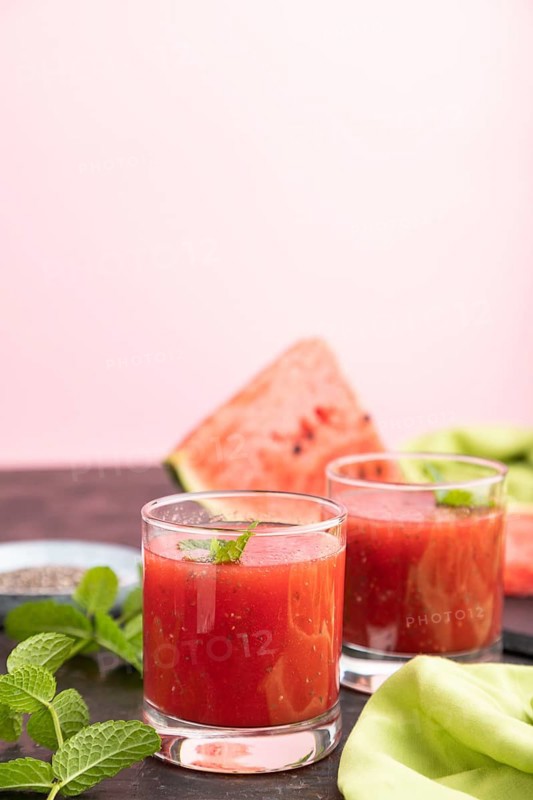 Watermelon juice with chia seeds and mint in glass on a black and pink background with green textile. Healthy drink concept. Side view, close up, selective focus, copy space