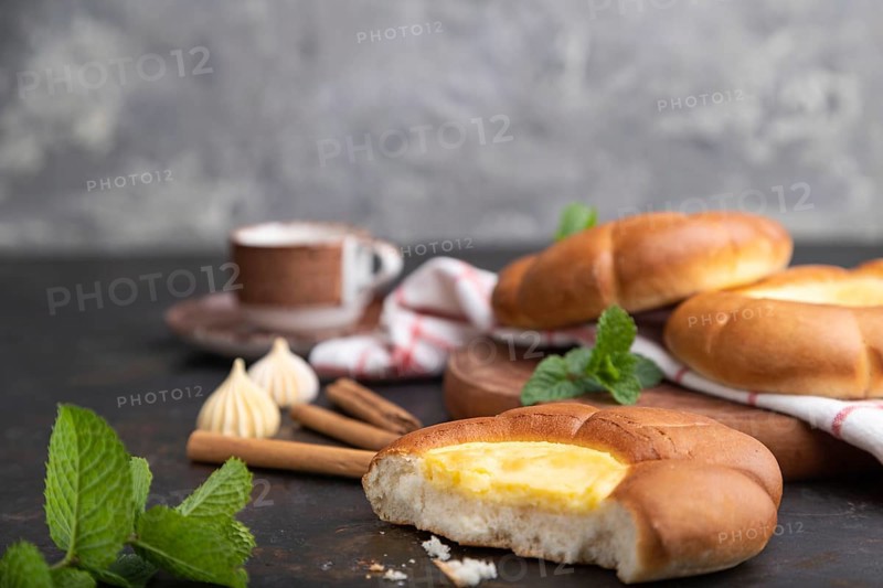 Sour cream bun with cup of coffee on a black concrete background and linen textile. Side view, close up, selective focus