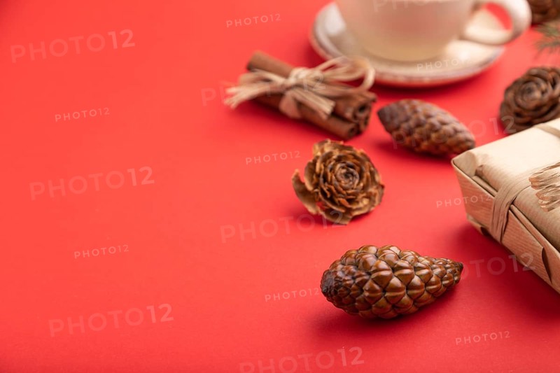 Christmas or New Year composition. Decorations, box, cinnamon, cones, fir and spruce branches, cup of coffee, on a red paper background. Side view, copy space