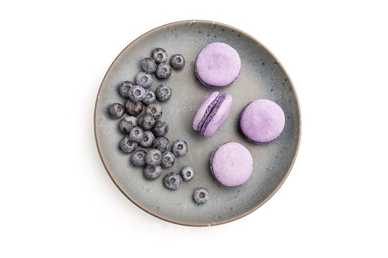 Purple macarons or macaroons cakes with blueberries on ceramic plate isolated on white background. Top view, flat lay, close up