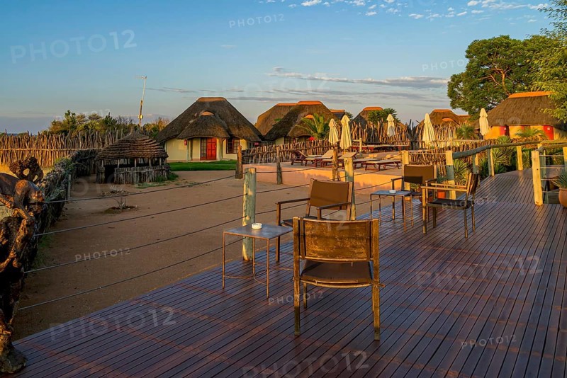 Sunset over African lodge with thatched roof huts and wooden terrace in the foreground, Namibia, Africa