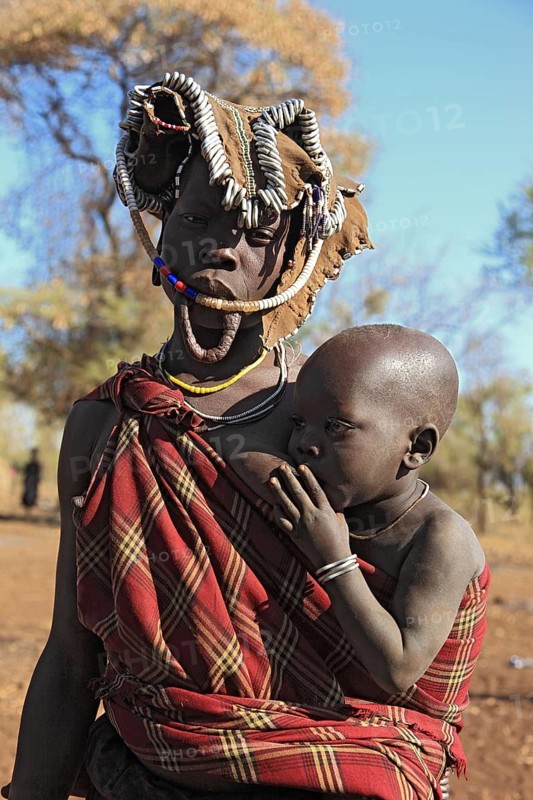 South Ethiopia, in Maco National Park, Mursi tribe, Mursi woman with baby, painted skin and headdress, baby drinking from breast, plate-lipped woman without plate, Ethiopia, Africa