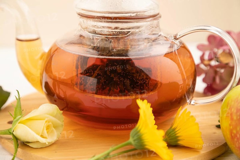 Red tea with herbs in glass teapot on white wooden background. Healthy drink concept. Top view, close up, selective focus
