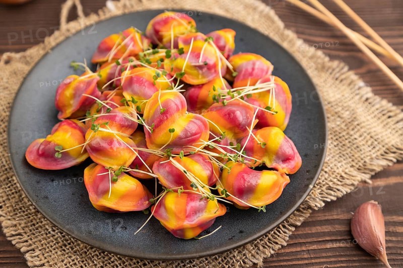 Rainbow colored dumplings with pepper, herbs, microgreen on brown wooden background and linen textile. Side view, close up, selective focus