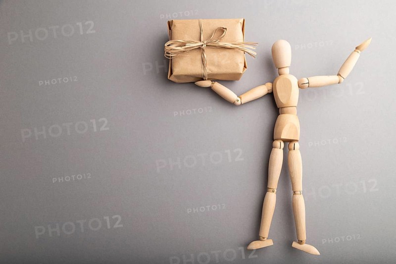 Wooden mannequin holding a gift box on gray pastel background. copy space, isolated, delivery concept