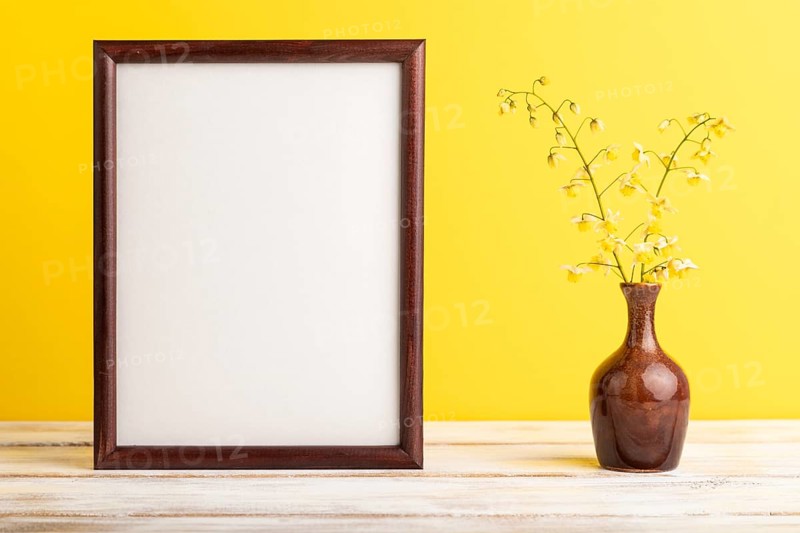 Wooden frame with yellow barrenwort flowers in ceramic vase on yellow pastel background. side view, copy space, still life, mockup, template, spring, summer minimalism concept