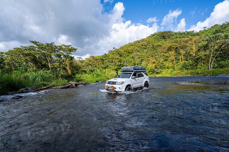 Toyota off-road vehicle with roof tent drives through a wide river in the rainforest, Alajuela province, Costa Rica, Central America
