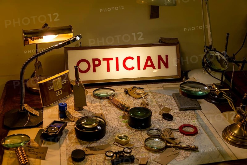 Optical items magnifying glasses labelled for sale with Optician illuminated sign, Marlesford Mill antiques centre, Suffolk, England, UK
