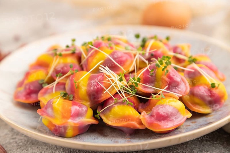 Rainbow colored dumplings with pepper, herbs, microgreen on brown concrete background and linen textile. Side view, selective focus