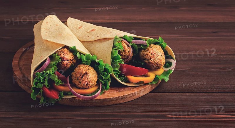 Tortillas wrapped with falafel balls and fresh vegetables, vegetarian healthy food, on a wooden background, no people