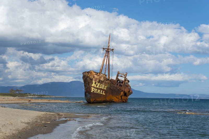 The bow of a rusty ship eats into the sandy beach against a blue sky and fluffy clouds, shipwreck Dimitrios, Glyfada beach, Selinitsa, Gythio, Githio, Gythion, Mani, Laconia, Peloponnese, Greece, Europe