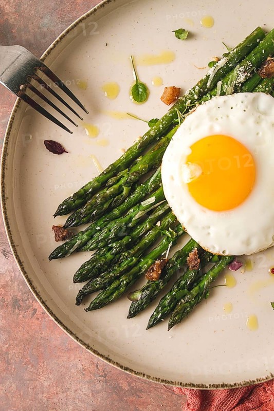 Grilled asparagus, with fried egg, spices and herbs, parmesan cheese, on a beige plate, top view, rustic, no people