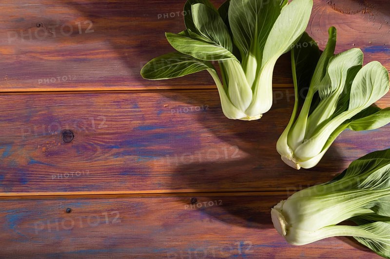 Fresh green bok choy or pac choi chinese cabbage on a colored wooden background. Hard light, contrast. Side view, copy space, selective focus