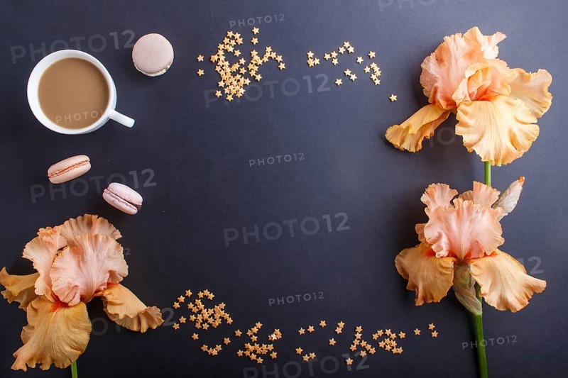 Orange iris flowers and a cup of coffee on a black background. Morninig, spring, fashion composition. Flat lay, top view, copy space
