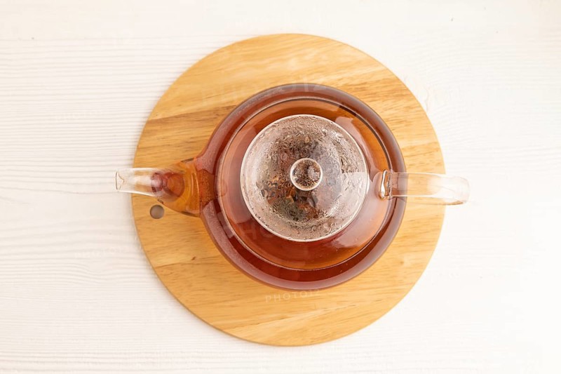 Red tea with herbs in glass teapot on white wooden background. Healthy drink concept. Top view, flat lay, close up