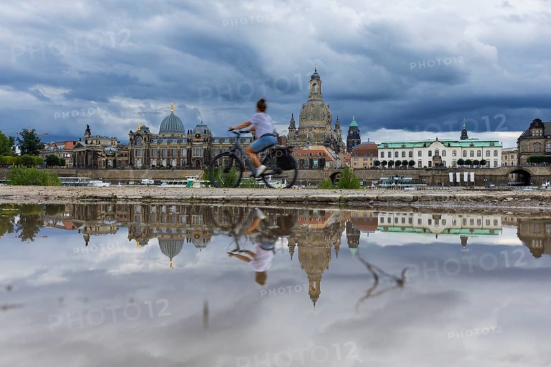 The Dresden silhouette with a cyclist and dark clouds behind the Church of Our Lady is reflected in a puddle on the Elbe cycle path, Elbe cycle path, Dresden, Saxony, Germany, Europe