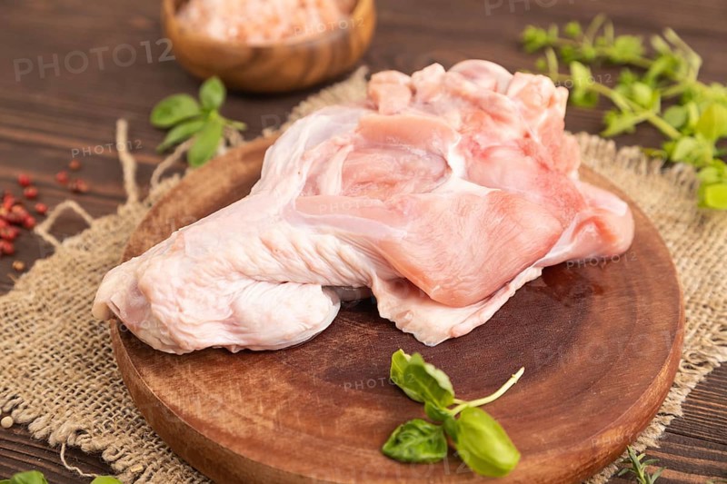 Raw turkey wing with herbs and spices on a wooden cutting board on a brown wooden background and linen textile. Side view, close up, selective focus