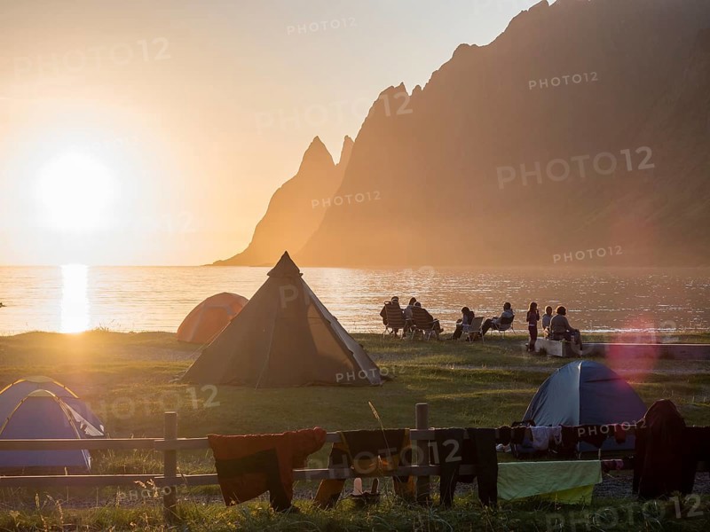 Beach Ersfjordstranden, fjord Ersfjord, people sitting in small groups at the beach, public recreation area, sunset, view to mountain range Okshornan, island Senja, Troms, northern Norway, Norway, Europe