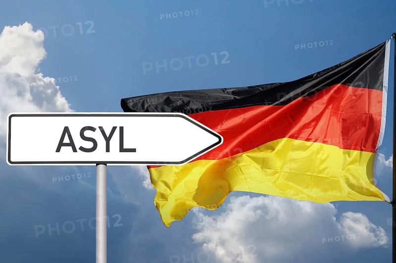 Sign with the inscription Asylum points in the direction of the German flag (symbolic image, composing)