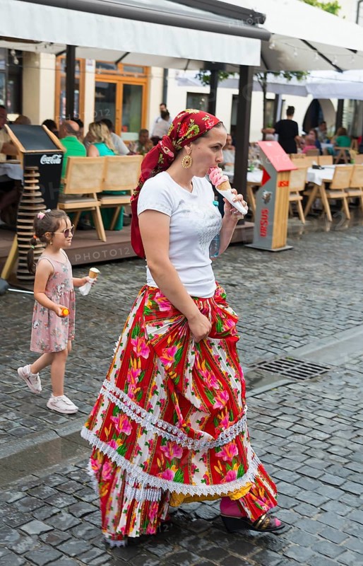 Woman in traditional dress eating ice cream on a busy street, child in the background, young woman in traditional dress, Sibiu, Transylvania, Romania, Europe