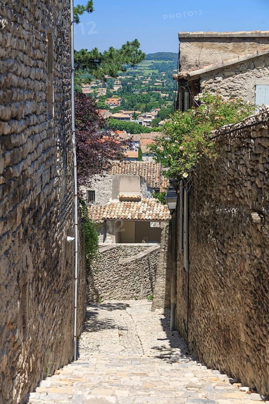 Stony alley in a village with views of houses and countryside in the distance, Vaison-la-Romaine, Provence, France, Europe