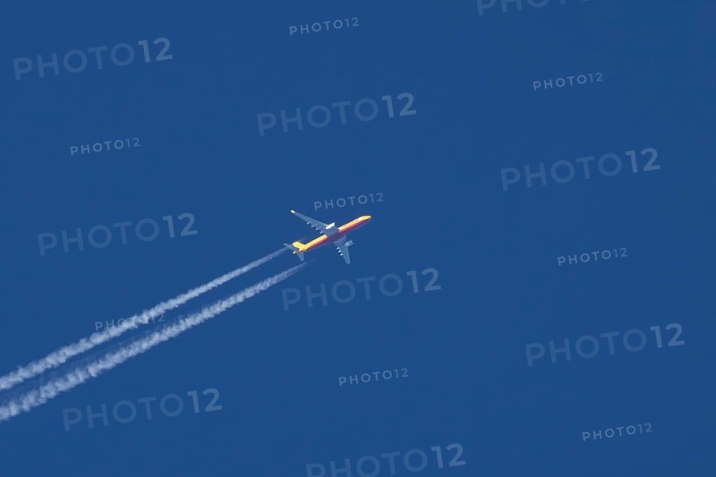Boeing 767 jet cargo aircraft of DHL flying in a blue sky with vapor trails or contrails behind, England, United Kingdom, Europe