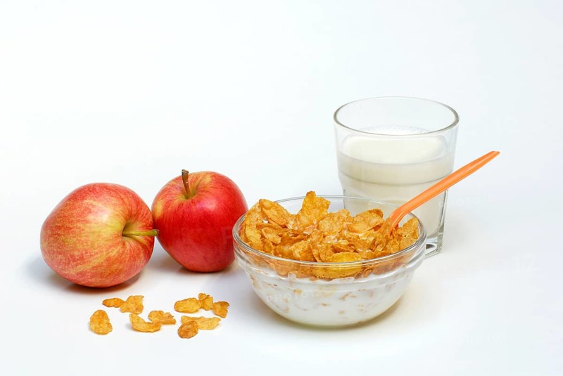 Glass bowl with cornflakes, apples, glass with milk, spoon, bowl