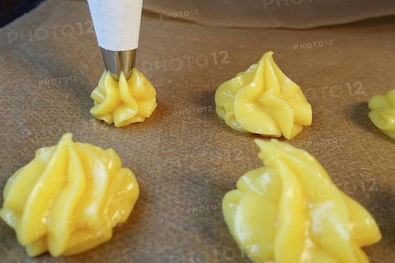Swabian cuisine, preparation of mini cream puffs, press raw choux pastry through piping bag onto baking paper, eclairs, profiteroles, piped pastries, oven cakes, choux pastries, pastry, hearty, salty, choux pastry, baked, from the oven, vegetarian, baking, typical Swabian reinterpreted, party pastries, finger food, appetisers for on the go, traditional cuisine reinterpreted, food photography, studio, Germany, Europe