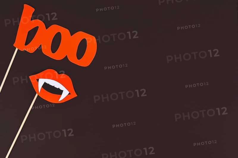 Halloween background with photo props on sticks in shape of red word boo and mouth with vampire teeth on dark background with copy space