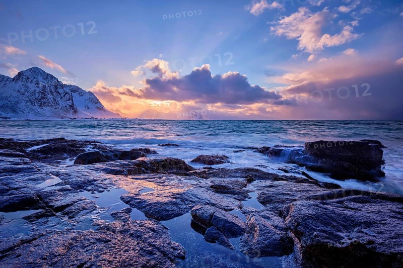Waves of Norwegian sea on rocky coast in fjord on sunset with sun. Skagsanden beach, Lofoten islands, Norway, Europe