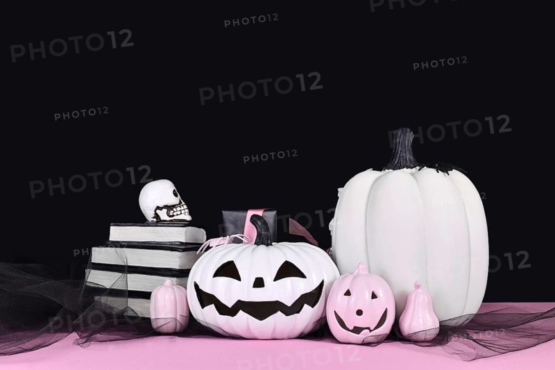 Pink and white Halloween decor with black and white pumpkins, spell books and spiders on black background with copy space