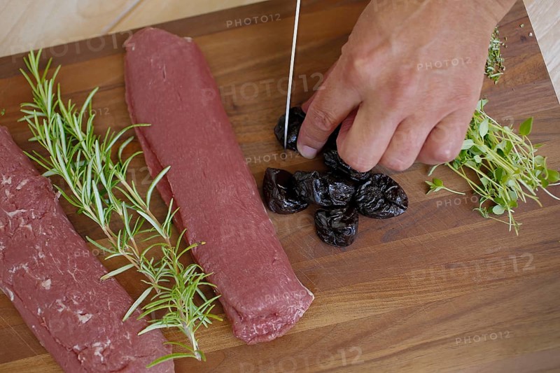 Swabian cuisine, preparation of lamb with prunes, raw lamb, rosemary, herbs, sliced garlic, lemon zest, fillets on wooden board, cutting prunes, kitchen knife, grandmother's kitchen, regional, home cooking, typical Swabian, traditional cuisine reinterpreted, food photography, man's hand, studio, Germany, Europe