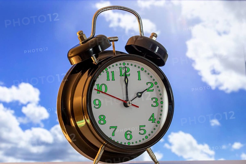 Symbolic image of the time change to summer time: close-up of an alarm clock in front of a blue sky