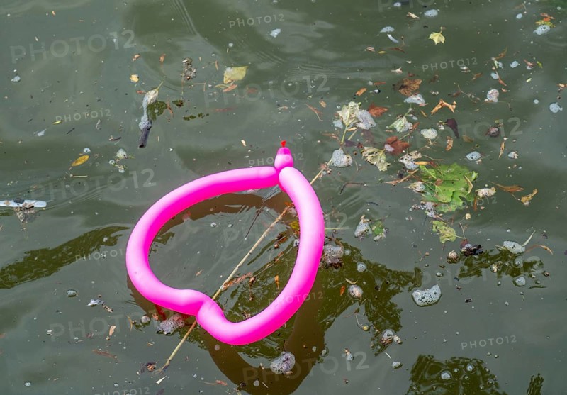 Pink balloon, shaped like a heart, floats in a dirty river
