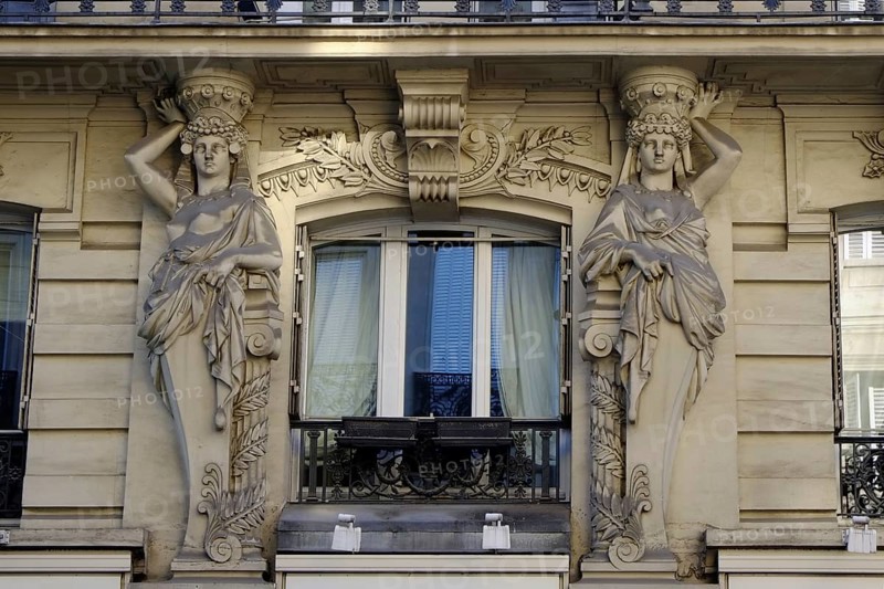 Two stone caryatids frame a window in the façade of a house in Paris as a decorative element. Landscape format. Two stone caryatids frame a window in the facade of a house in Paris as a decorative element. Horizontal format