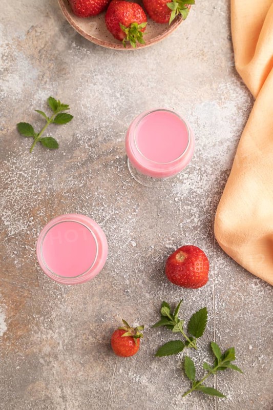 Sweet strawberry liqueur in glass on a gray concrete background and orange textile. top view, flat lay
