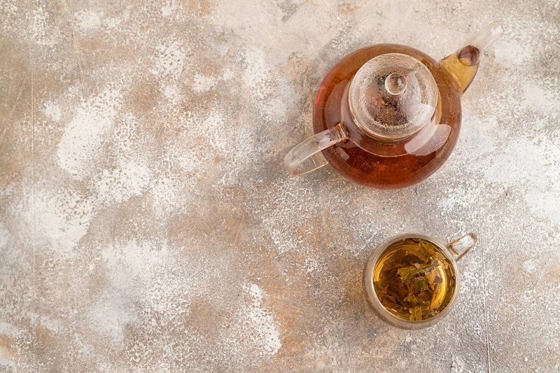 Red tea with herbs in glass teapot on brown concrete background. Healthy drink concept. Top view, flat lay, copy space