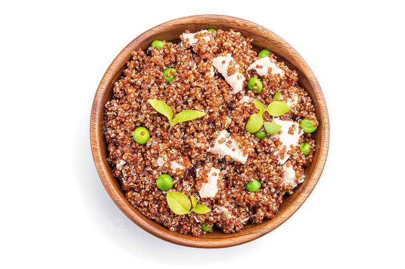 Quinoa porridge with green pea and chicken in wooden bowl isolated on a white background. Top view, flat lay, close up