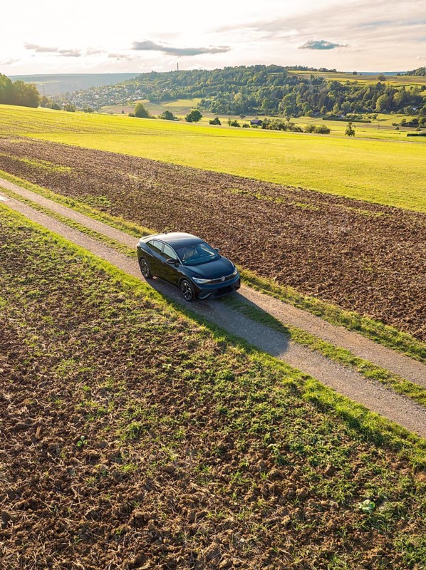 A car drives on a dirt track between large fields under a sky with clouds and evening sun, car sharing, VW ID5, Calw, Black Forest, Germany, Europe