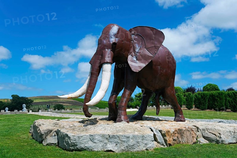 Metal sculpture of an elephant on a rock foundation in a green park under a blue sky with white clouds, Bacalhôa, Bacalhoa Buddha Eden, Quinta dos Loridos, largest oriental garden in Europe, Bombarral, Oeste, Centro, Portugal, Europe