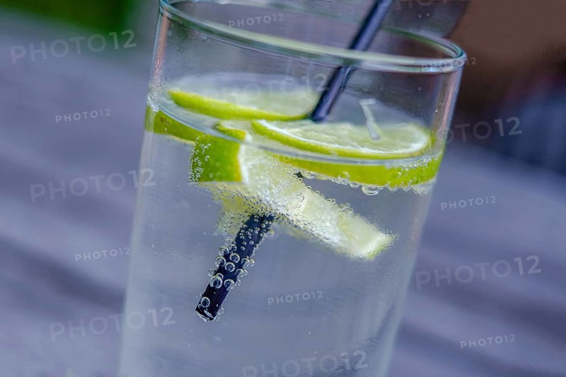 Glass with mineral water, lemon slices and straw