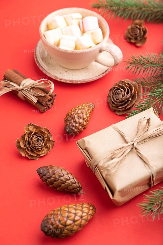 Christmas or New Year composition. Decorations, box, cinnamon, cones, fir and spruce branches, cup of coffee, on a red paper background. Side view, close up
