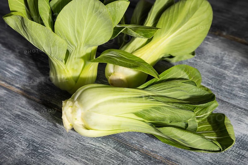 Fresh green bok choy or pac choi chinese cabbage on a gray wooden background. Hard light, contrast. Side view, close up