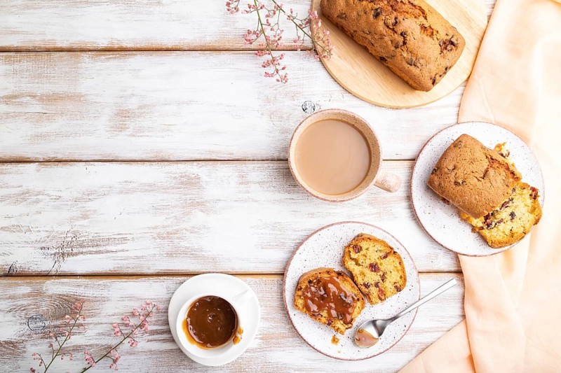 Homemade cake with raisins, almonds, soft caramel and a cup of coffee on a white wooden background and orange linen textile. top view, flat lay, copy space