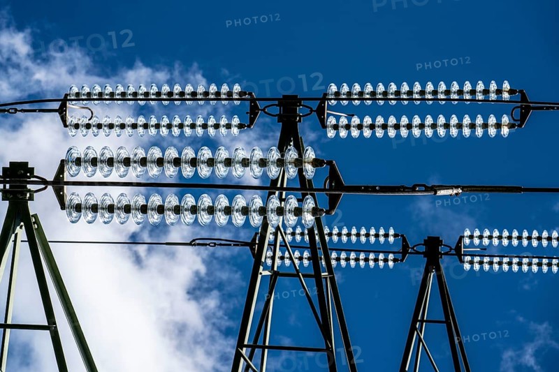 Insulators made of glass on a high-voltage line, they hang on the pylons as a suspension device between the pylon and the live, non-insulated cable, extra-high voltage line, symbolic image energy