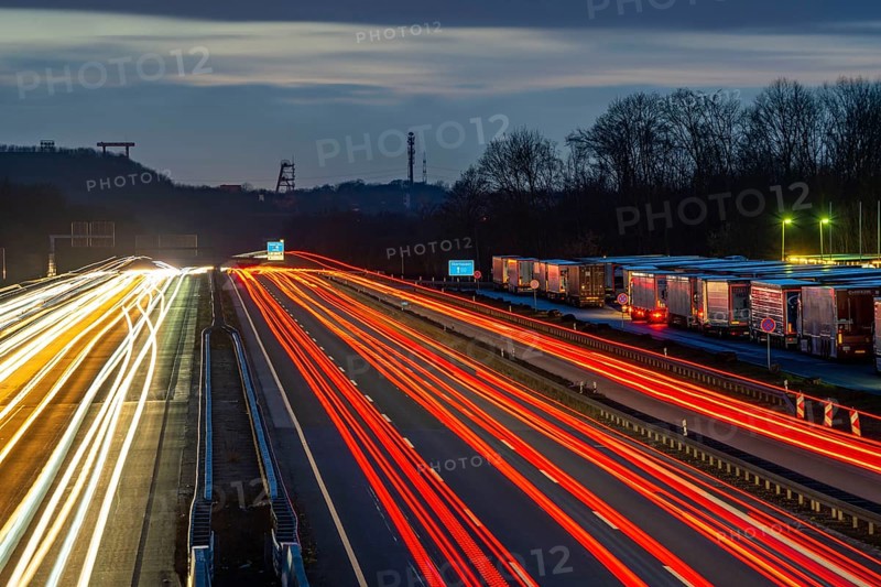 Evening traffic on the A2 motorway at the Recklinghausen junction heading west, in the background the headframes of the former Ewald colliery, Hohenhorst rest area, overflowing with lorries, North Rhine-Westphalia, Germany, Europe